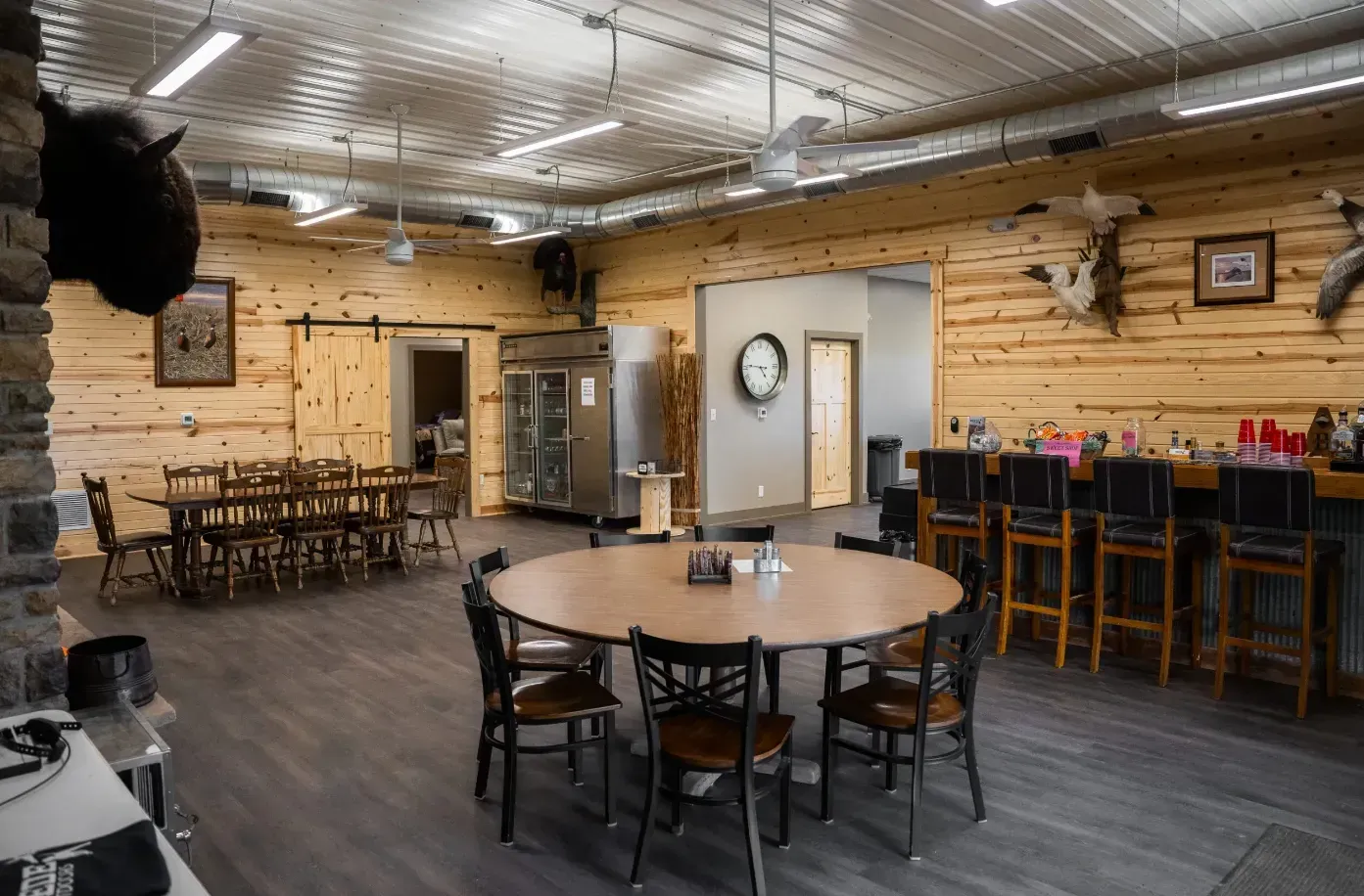 Rustic event space with wood paneling, bar, tables, and animal mounts.