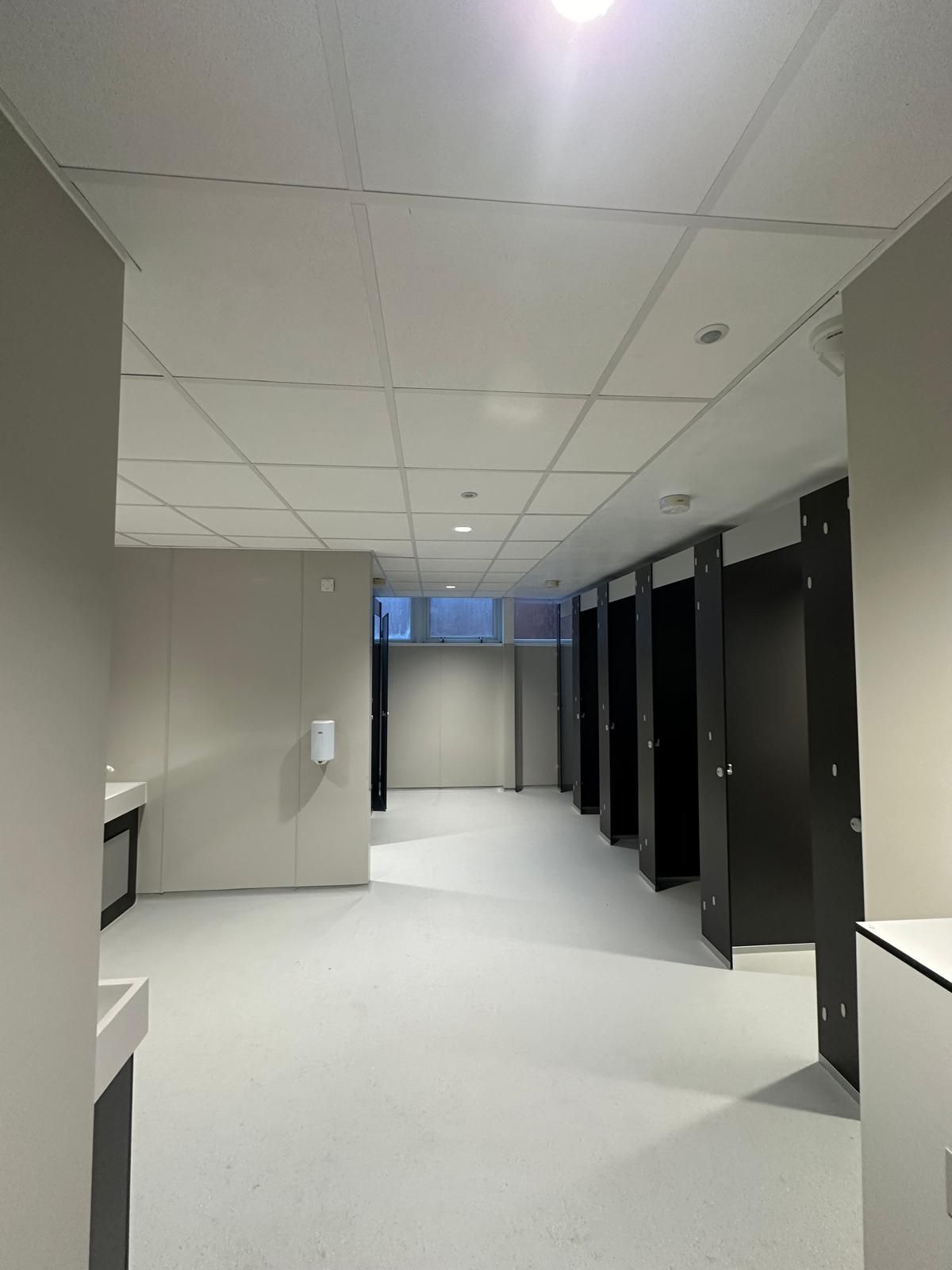 A large empty room with a lot of cubicles and a sink.