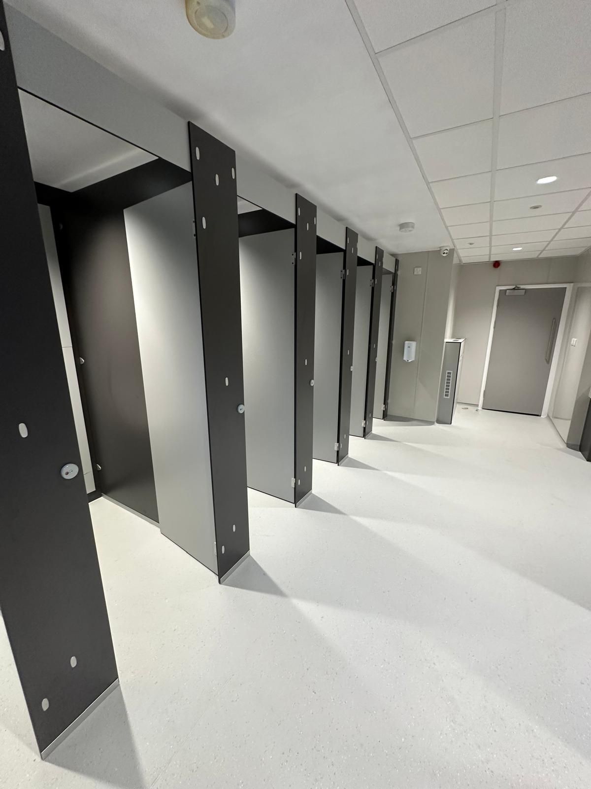 A long hallway with a row of toilet cubicles in a building.