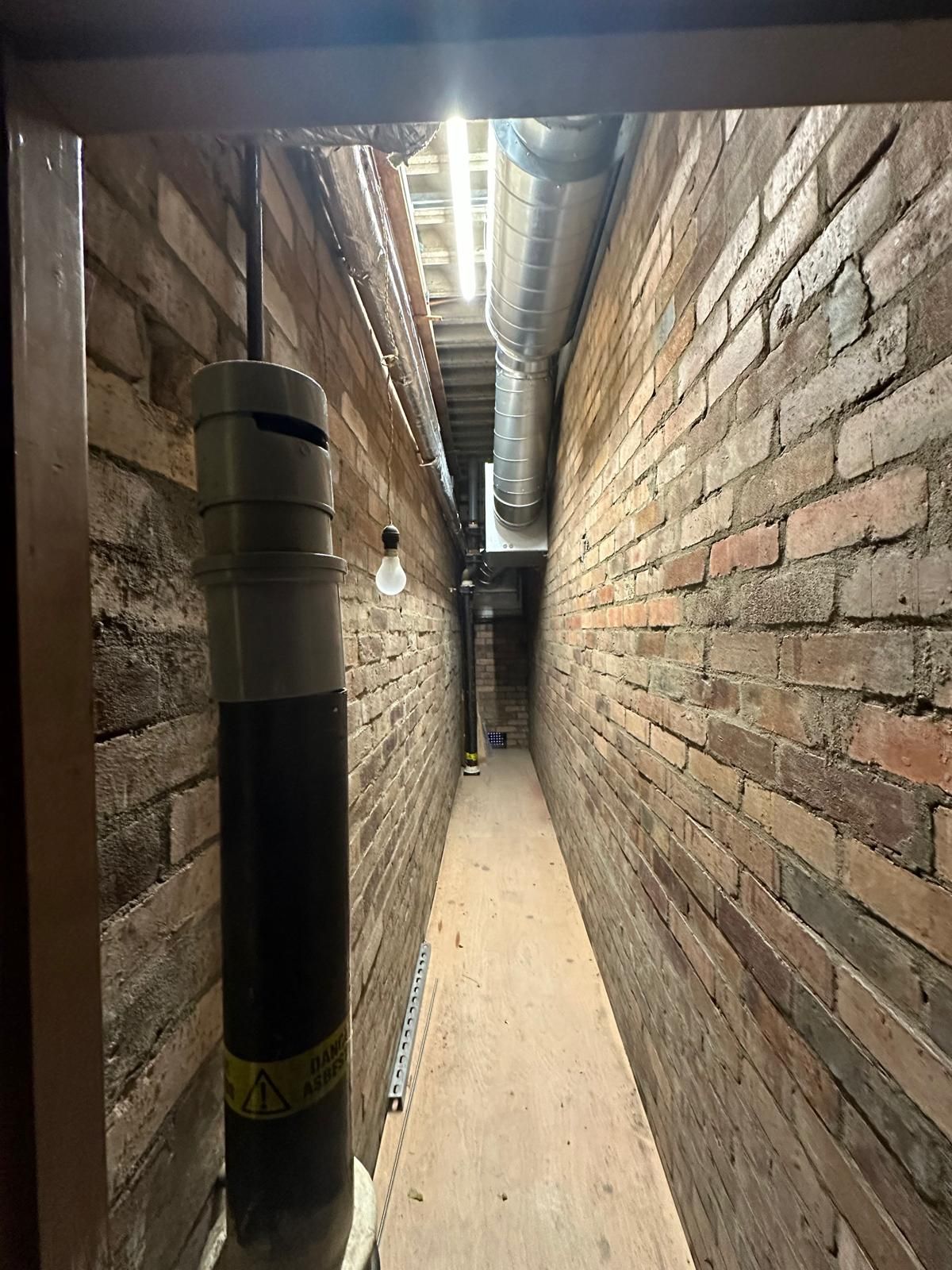 A long narrow hallway with brick walls and pipes.