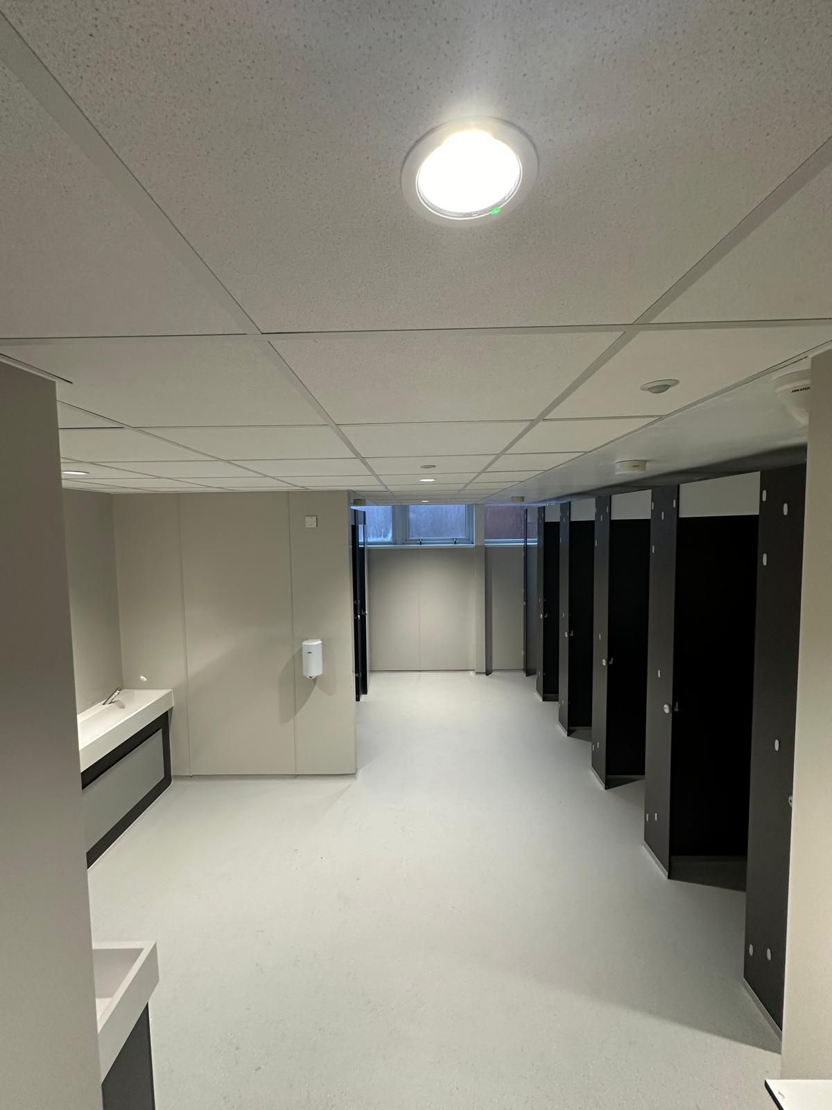 A bathroom with a row of stalls and a sink.