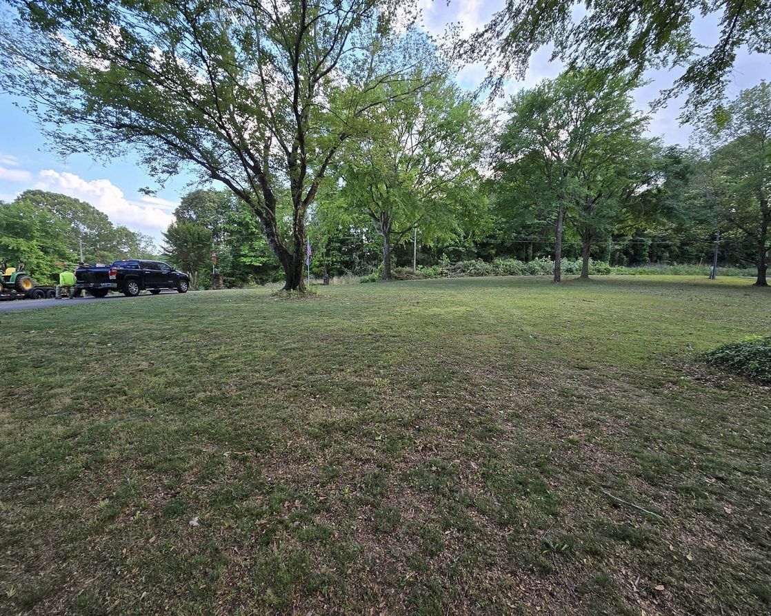 A large grassy field with trees and a truck parked in the background.