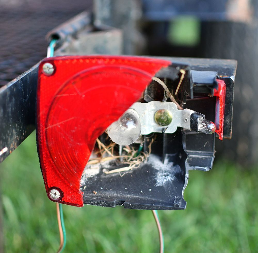 Damaged trailer tail light, red lens partially broken, bulb exposed, wires visible.