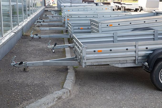 Rows of new metal trailers parked outside a building with a glass facade.