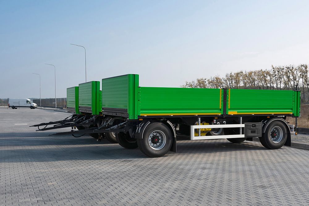 Three green flatbed trailers parked on a concrete surface.