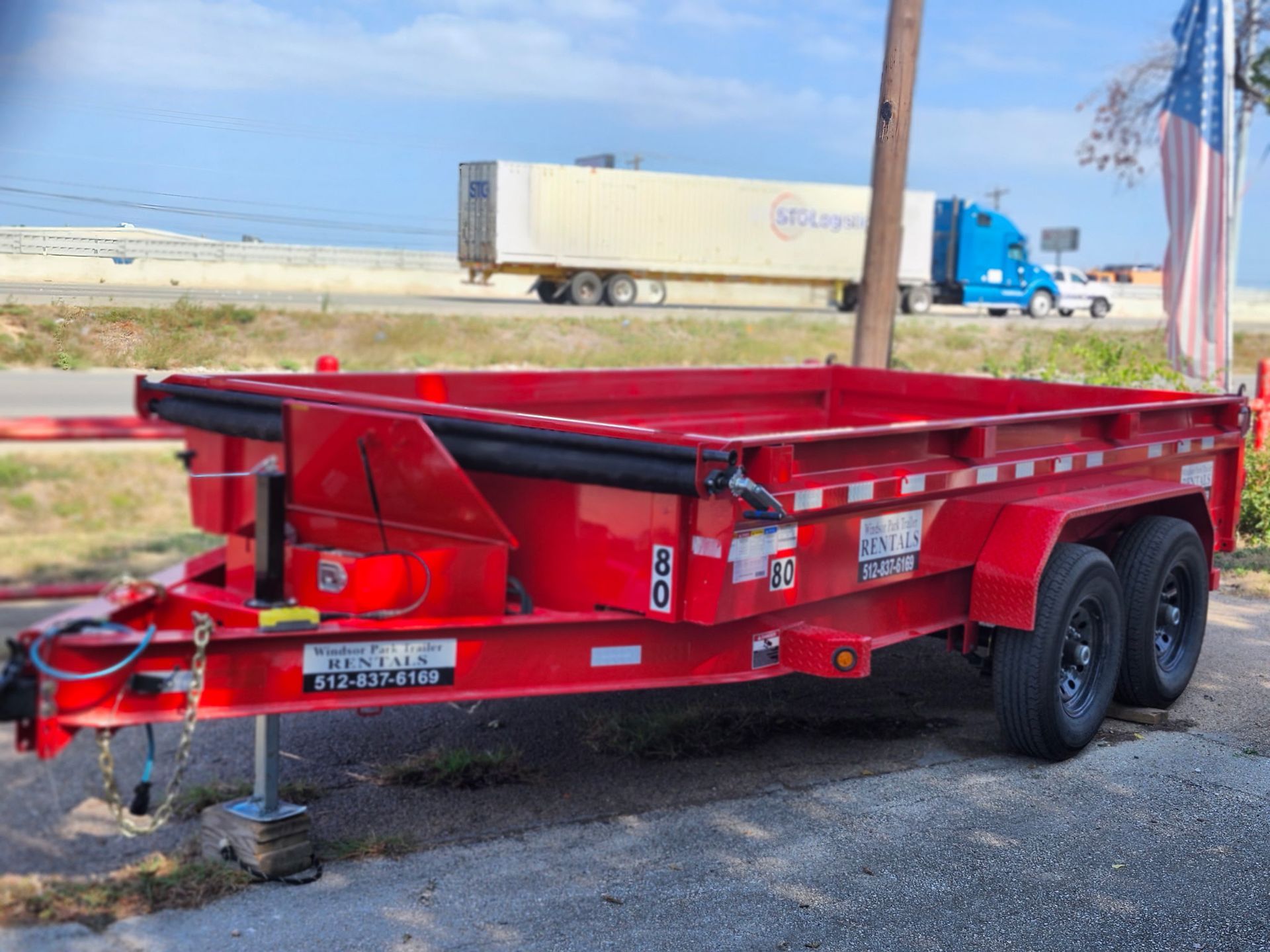 Gray utility trailer with metal cage hitched to a black car on a gravel driveway.