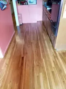 Hardwood floor hallway with pink and brown walls, leading to a kitchen with dark cabinets.