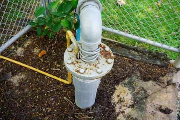A metal pipe assembly connected to a wellhead on the ground, with a yellow cable looping through a bolted flange.