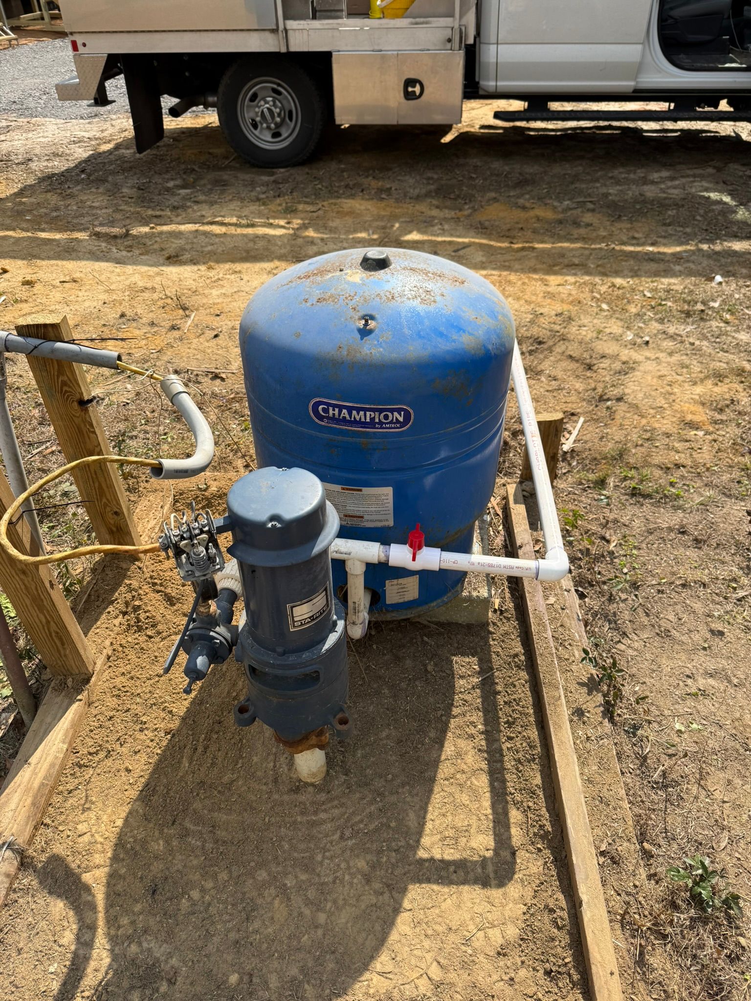A blue well pressure tank and pump system installed outdoors on a gravel ground surface.