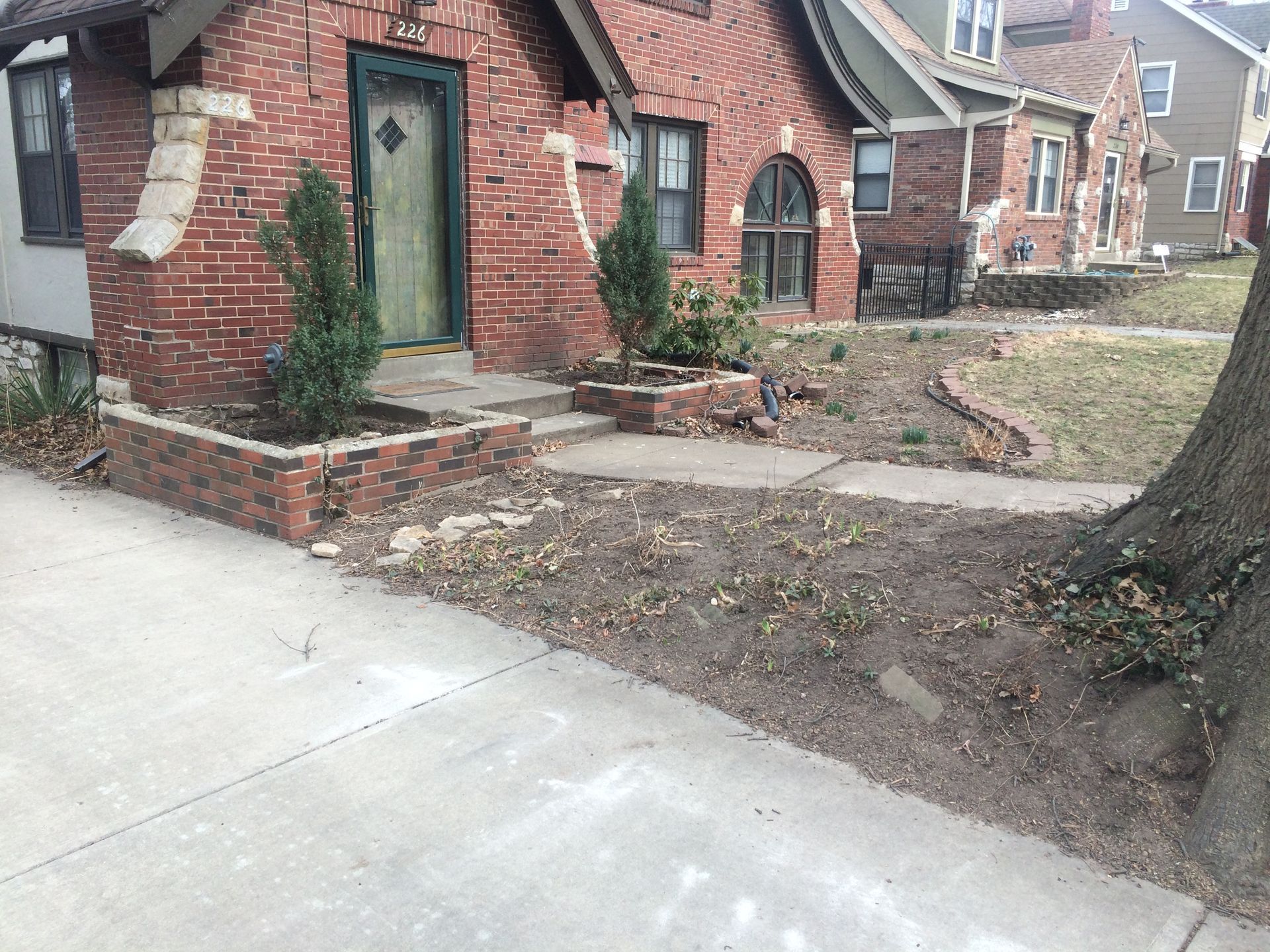 A brick house with a front entryway, brick planter boxes, a concrete walkway, and a tree in the front yard.