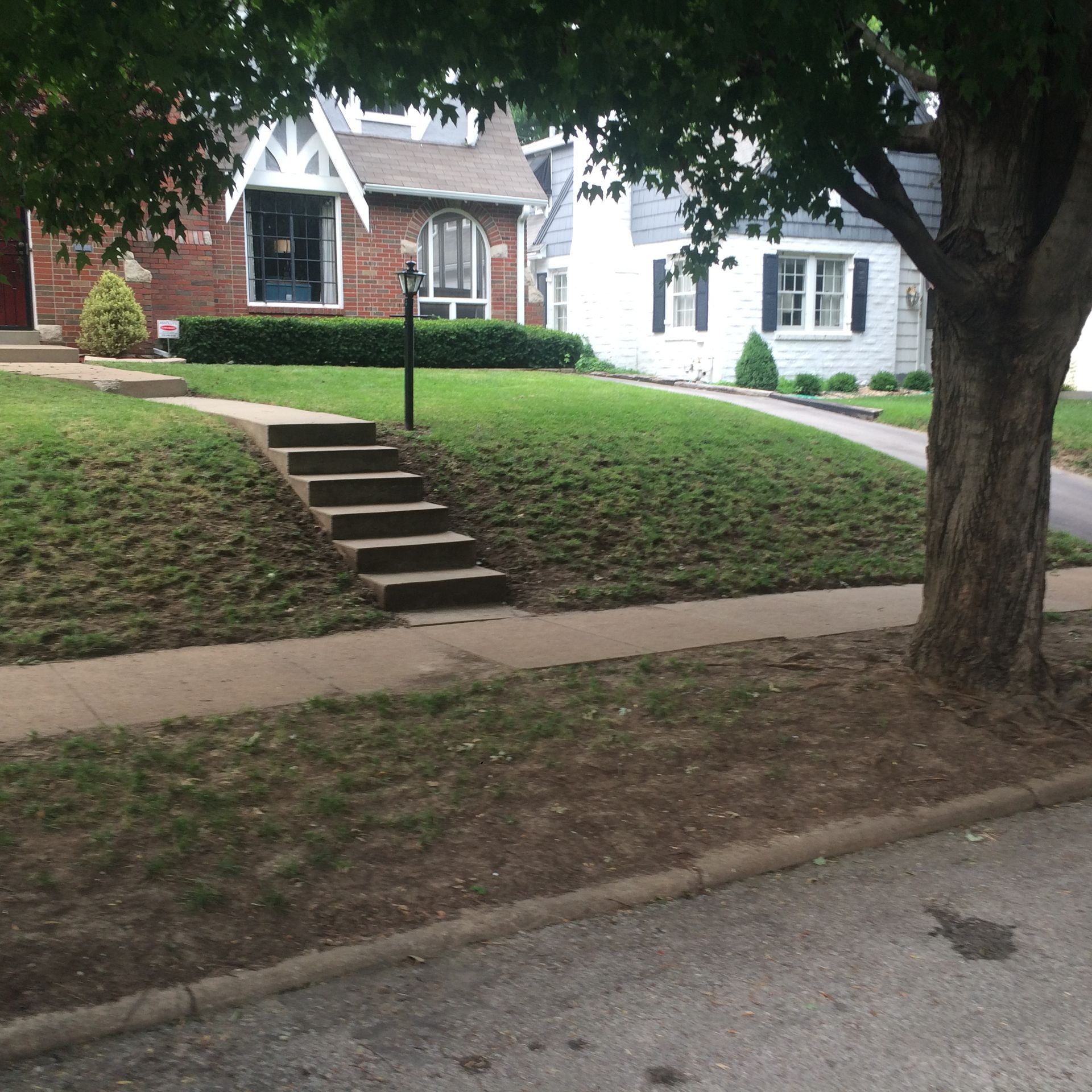 A brick house with a front lawn and a set of concrete stairs leading from the sidewalk to the home.