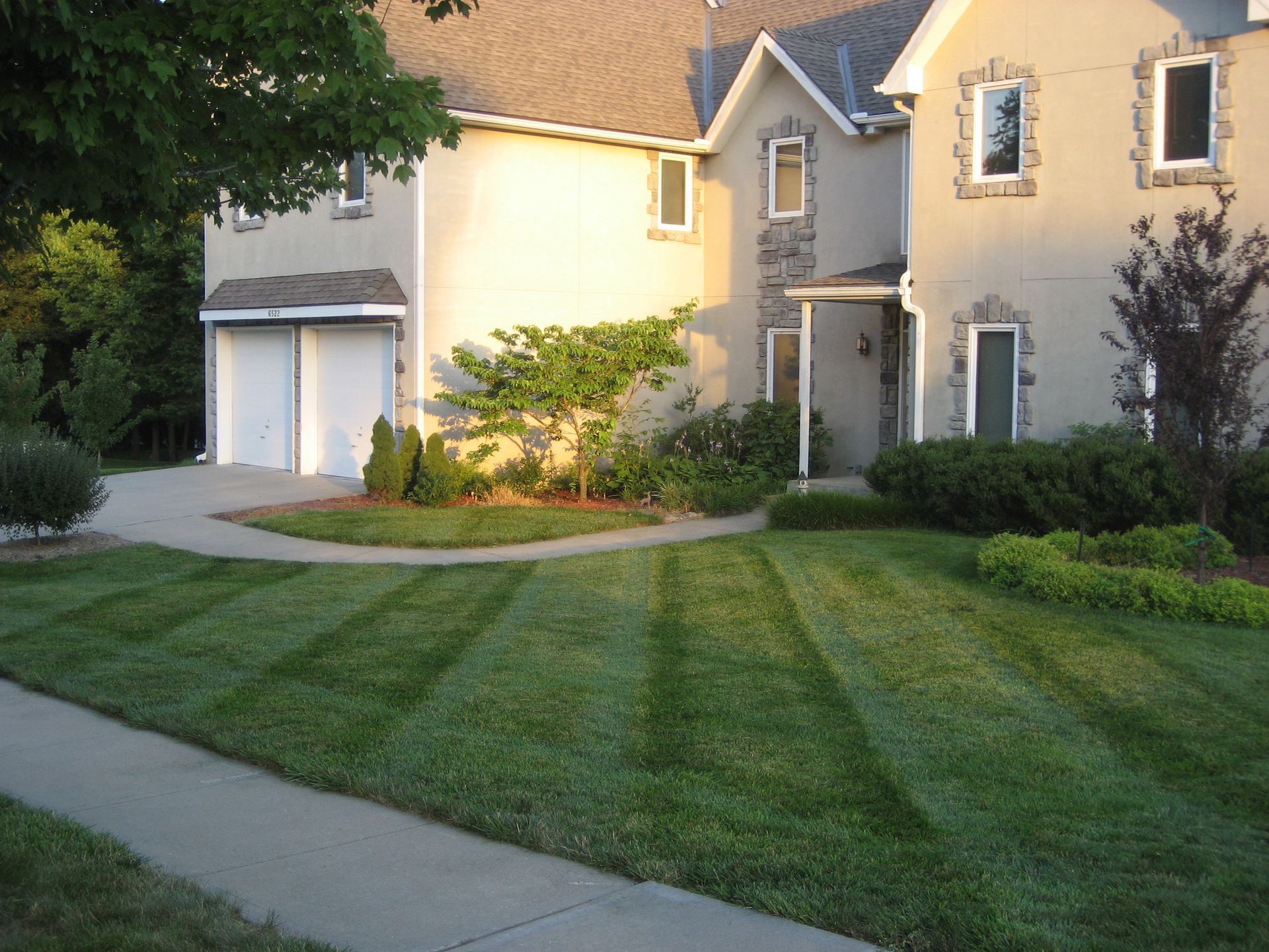 A two-story suburban house with a beige stucco exterior and a neatly mown lawn with striped patterns.