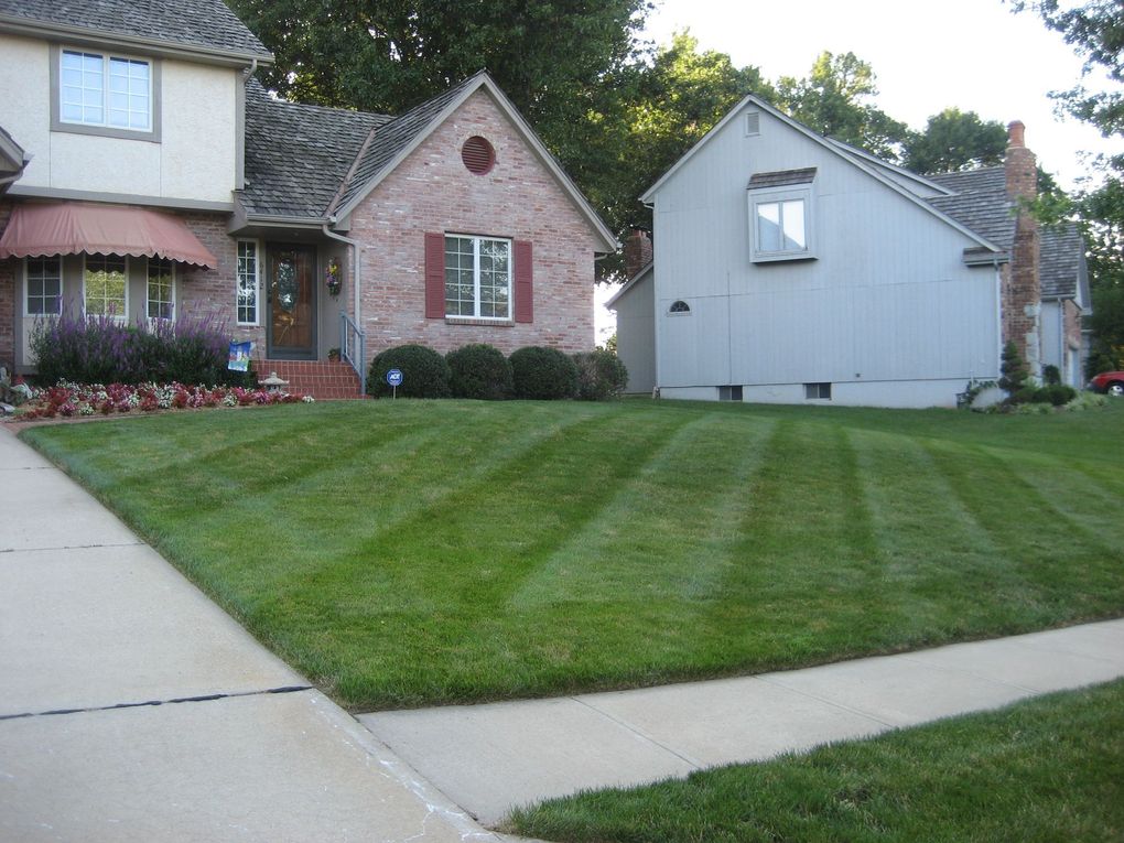 A manicured lawn with freshly mowed stripes in front of a brick house and a neighboring grey home.