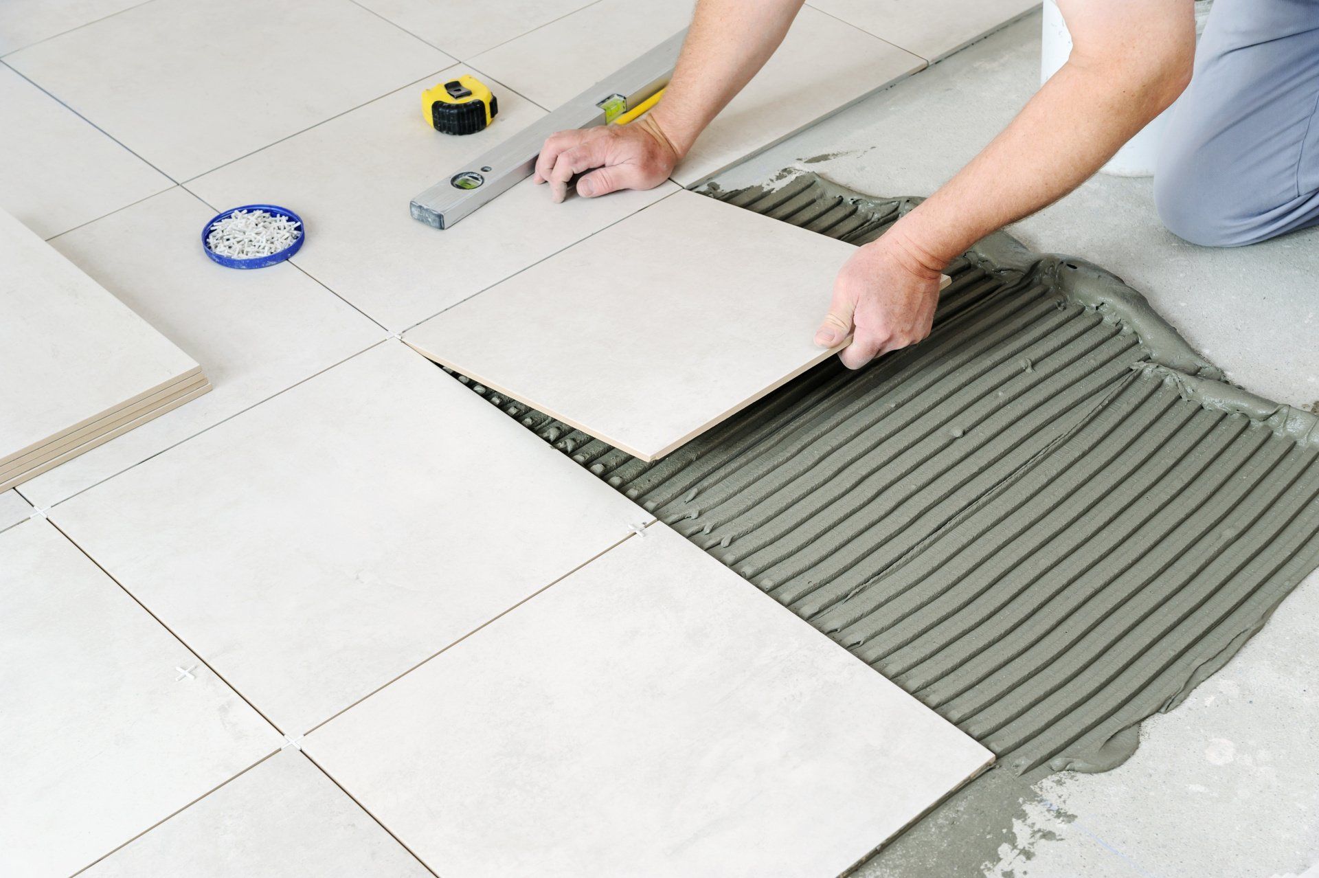 A person carefully installing ceramic tiles on a floor, creating a beautiful tiled surface.