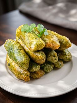 Stack of golden-green fried rolls garnished with cilantro on a white plate