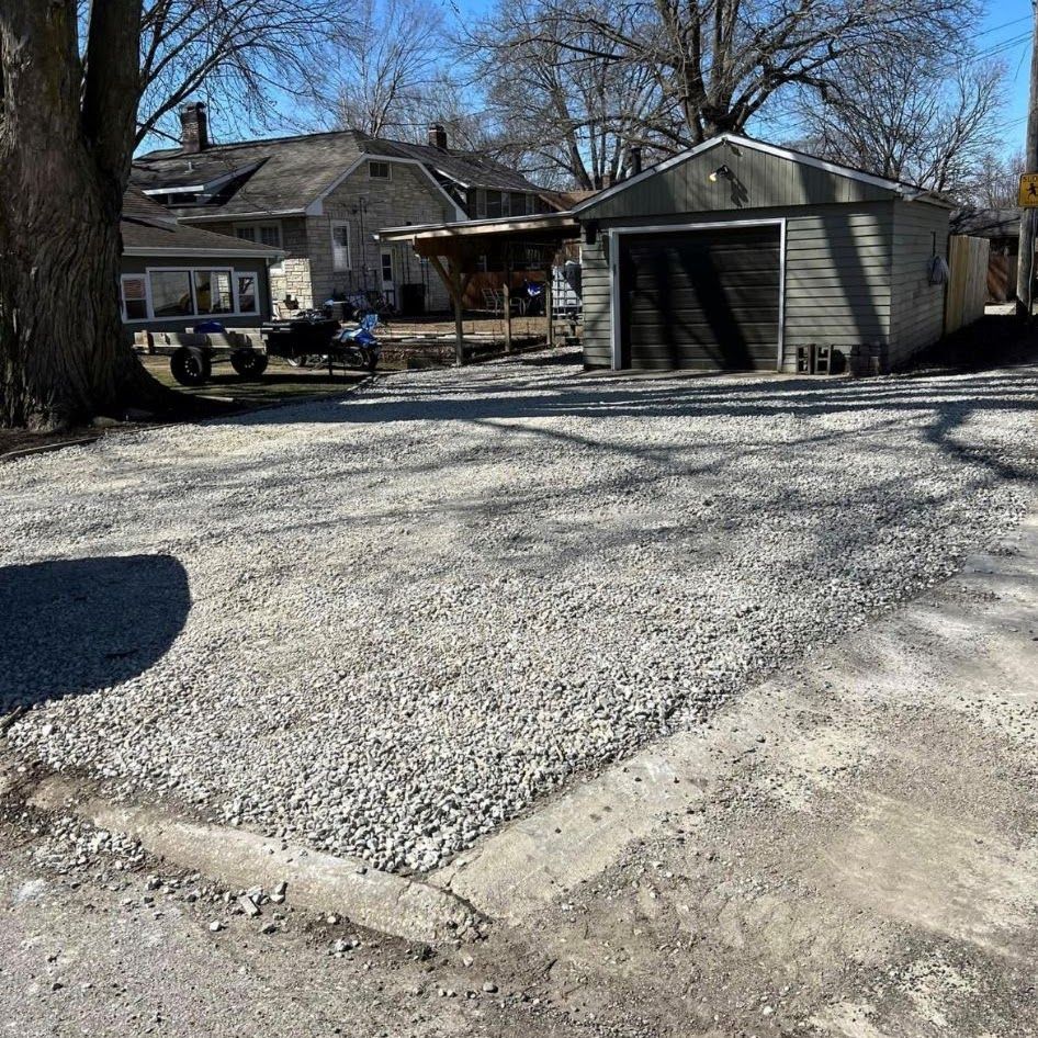A gravel driveway with a garage and a house in the background.