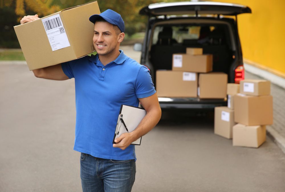 Delivery Man is Carrying a Box and a Clipboard in Front of a Van Filled With Boxes — Grants Express in Orange, NSW