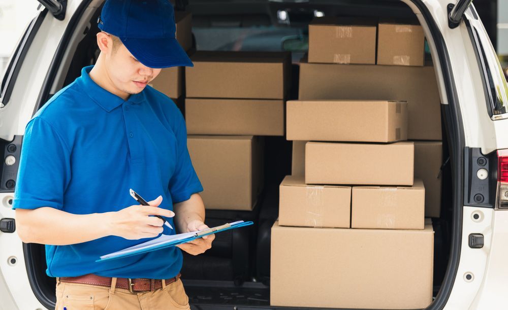 Delivery Man is Writing on a Clipboard in Front of a Car Filled With Boxes — Grants Express in Bathurst, NSW