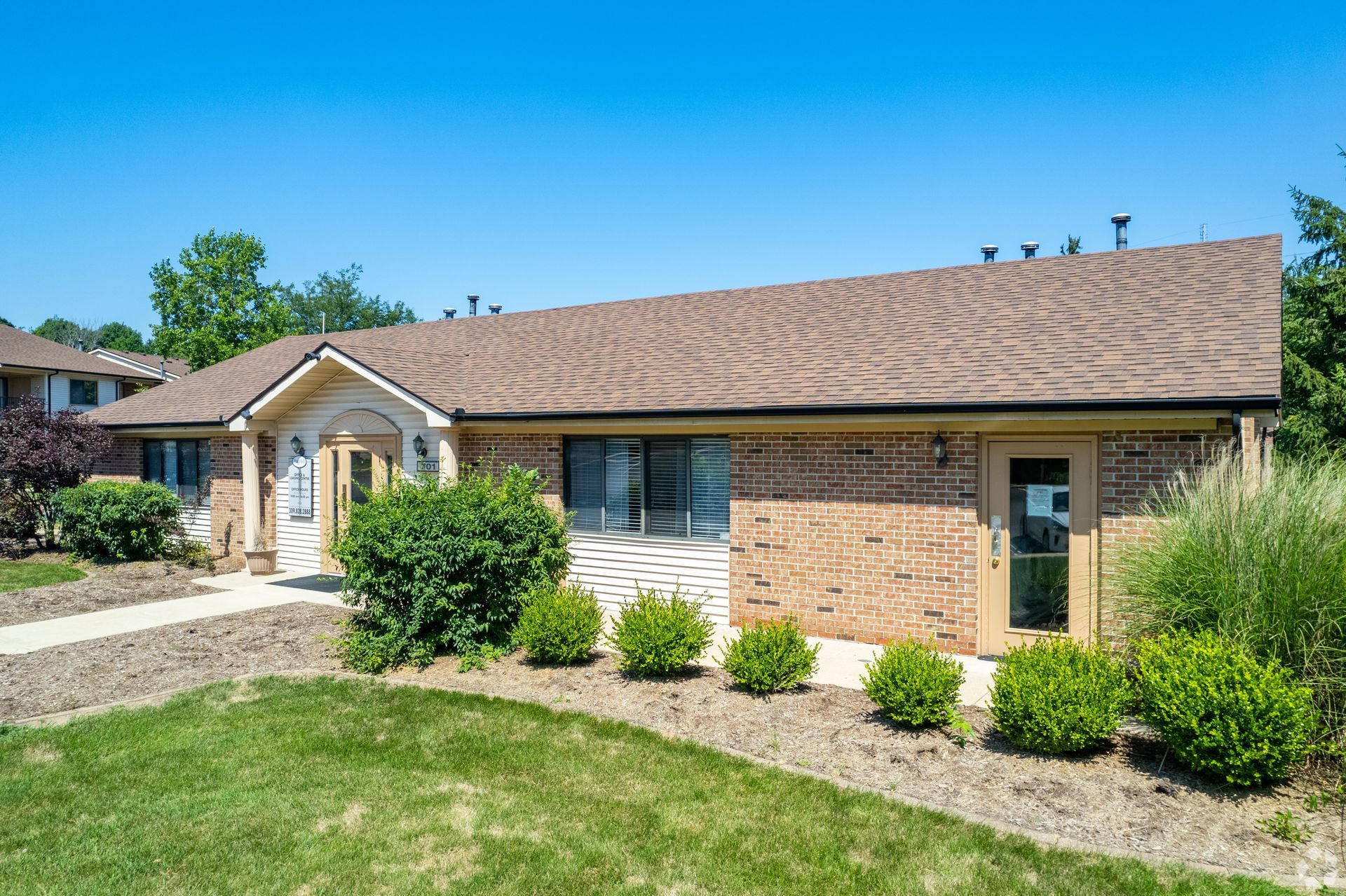 A brick house with a brown roof and a large lawn in front of it.