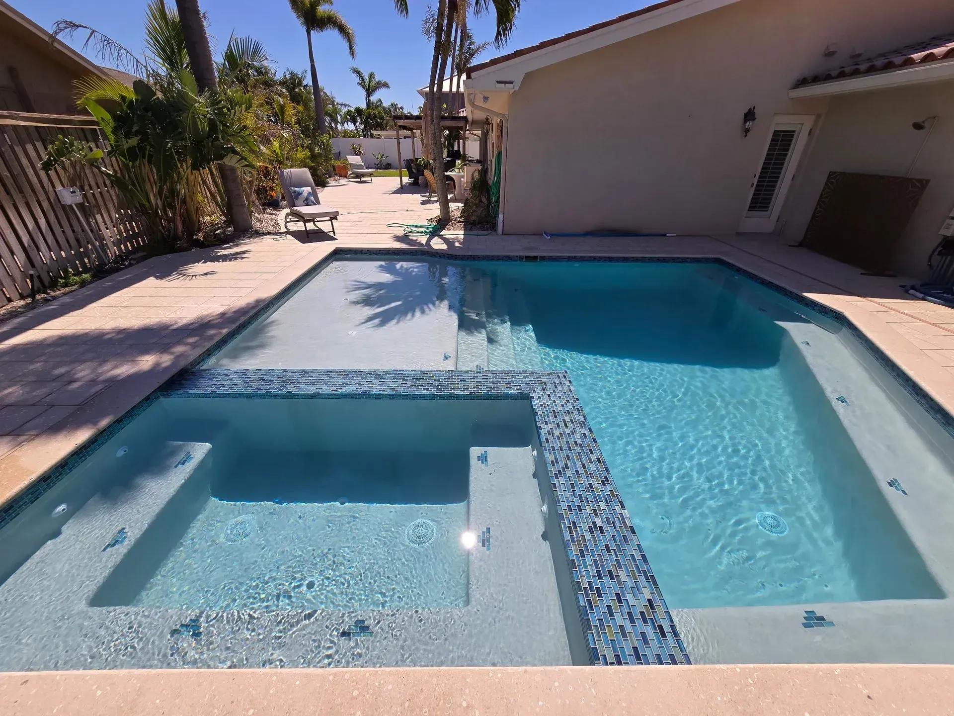 Backyard pool with hot tub, tropical plants, and lounge chair beside a tiled-roof house. Backyard pool with hot tub, tropical plants, and lounge chair beside a tiled-roof house.
