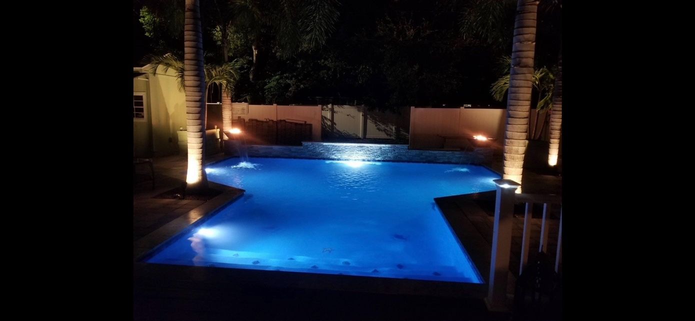 A large swimming pool is lit up at night with blue lights.