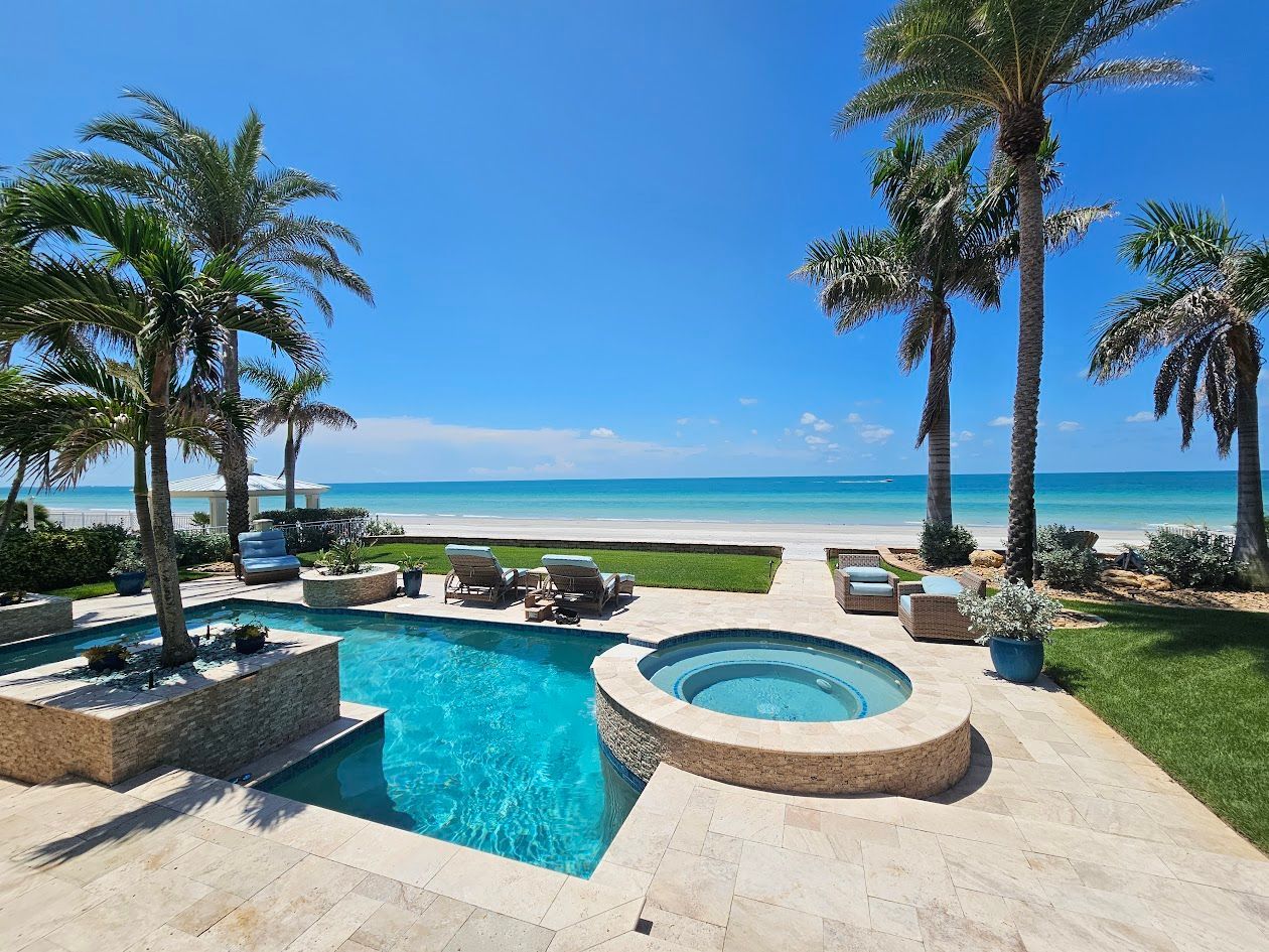A large swimming pool with a hot tub surrounded by palm trees and a view of the ocean.