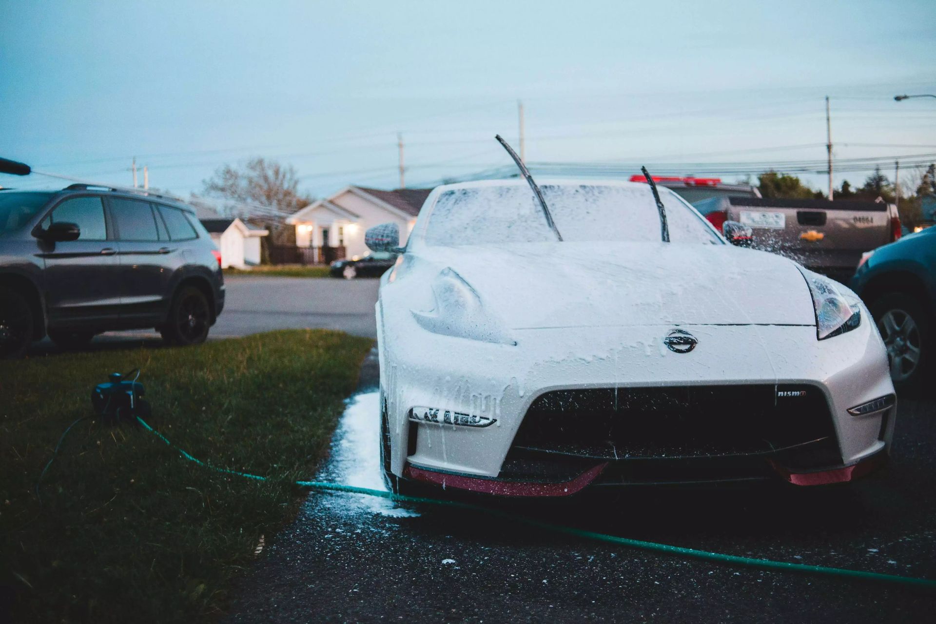 A white car is covered in foam in a parking lot.