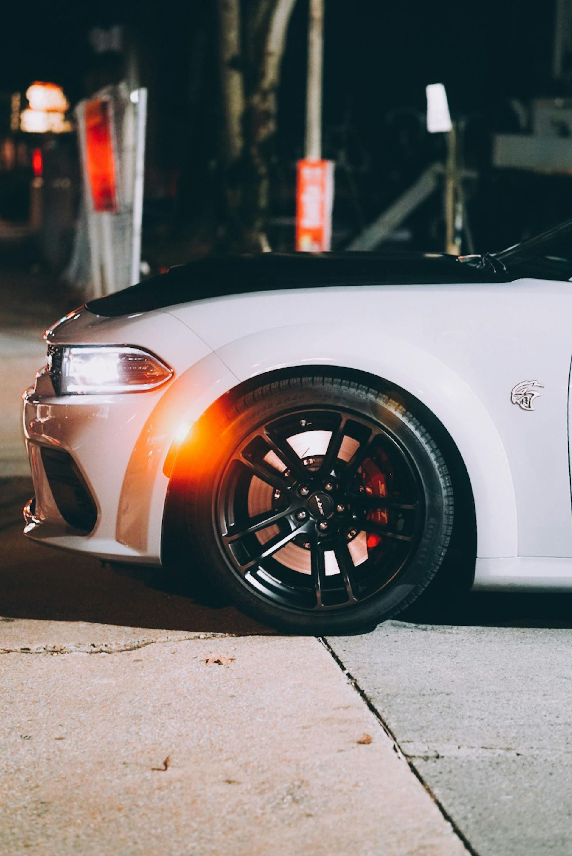 A white dodge charger is parked on the side of the road at night.