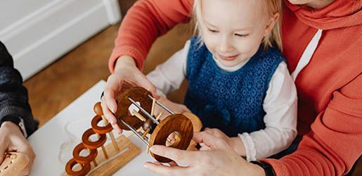 A child and adult playing with a wooden toy, smiling. Indoors, warm tones.