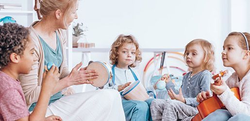 A music teacher and children play instruments together in a classroom.