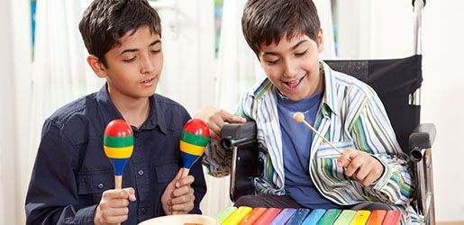 Two boys playing musical instruments, one in a wheelchair using a xylophone, the other with maracas.