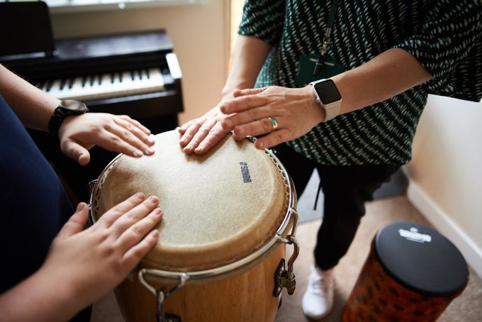 Two people's hands on a drum. A piano is in the background.