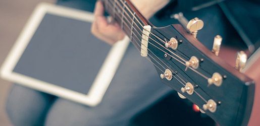 Acoustic guitar neck and headstock with tuning pegs, person holding tablet.