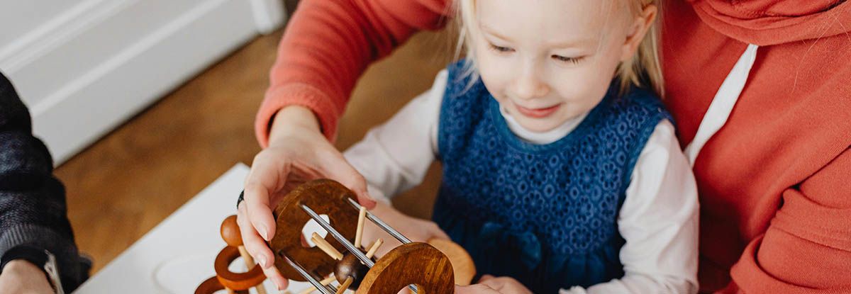 A young child smiles while building a gingerbread house with an adult's help.