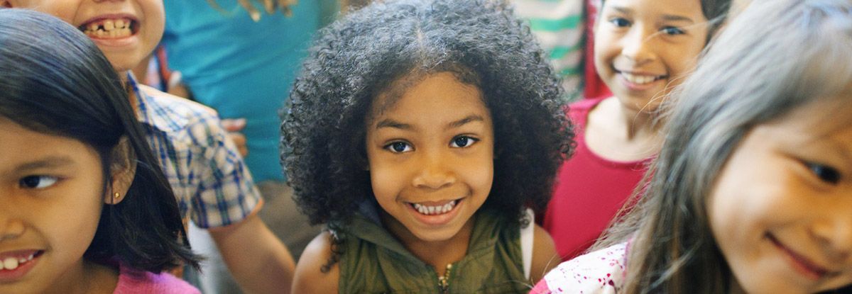 Group of smiling children, one with curly hair is in the center.