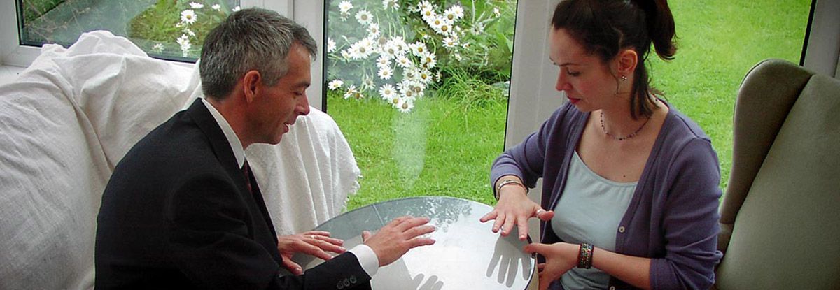 Man in a suit and woman in a cardigan are at a table in a well-lit room, conversing.