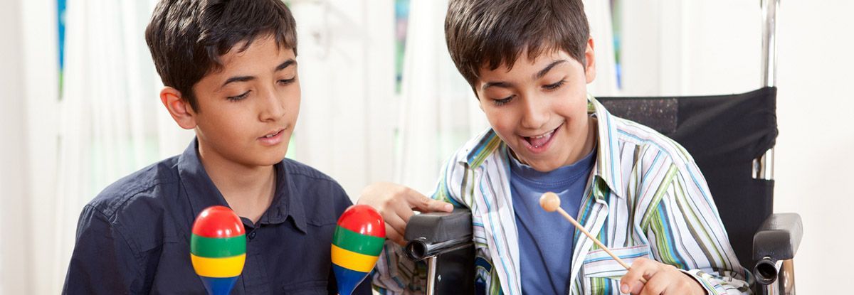 Two boys, one in a wheelchair, play maracas and smile.