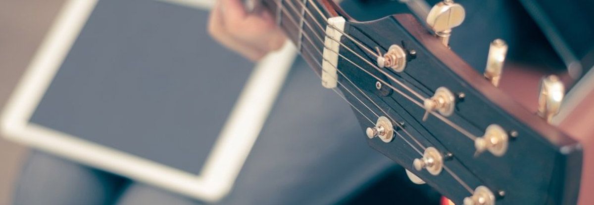 Acoustic guitar's headstock next to a tablet, suggesting music learning or performance with technology.