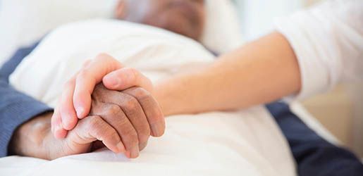 Two hands, one holding the other, resting on a white surface. One is in a blue coat. The other arm in a white shirt.