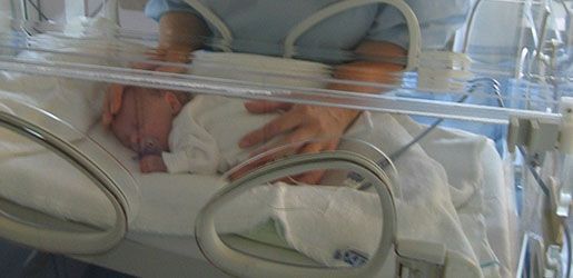 A mother with her newborn baby inside an incubator in a hospital.