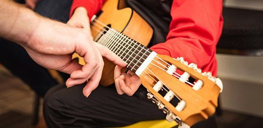 A person's hand guiding someone's fingers on the frets of a classical guitar, helping them learn.