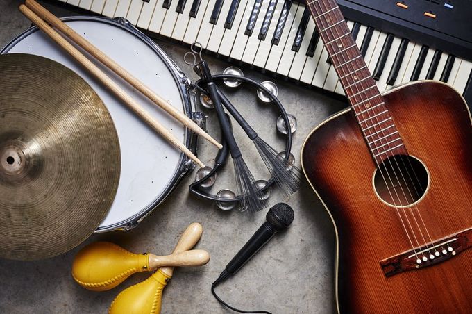 Musical instruments: drum, guitar, keyboard, cymbal, tambourine, microphone, and maracas on a gray surface.