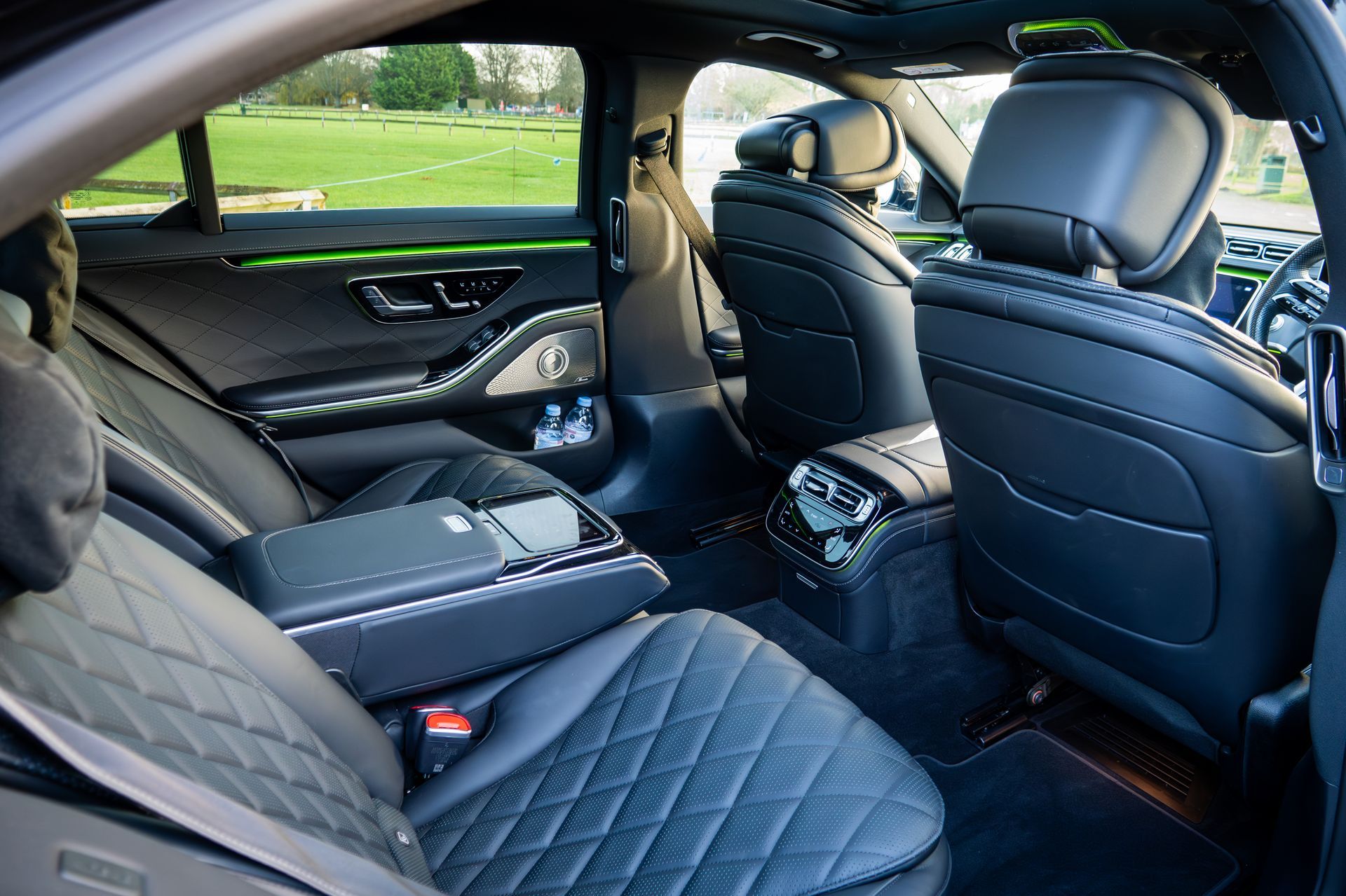 Black leather interior of a luxury car with diamond-patterned seats, armrest, and ambient lighting.