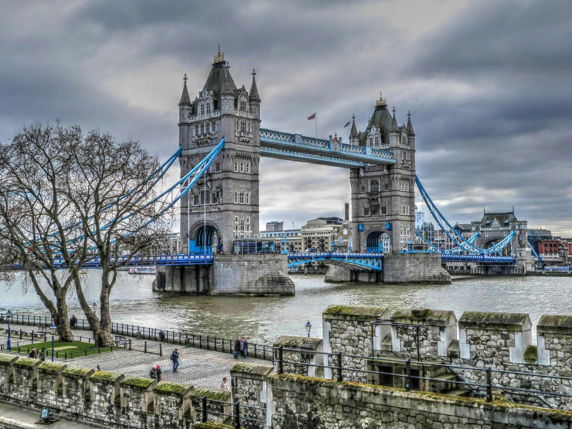 Tower Bridge in London on a cloudy day; water and stone wall in the foreground.