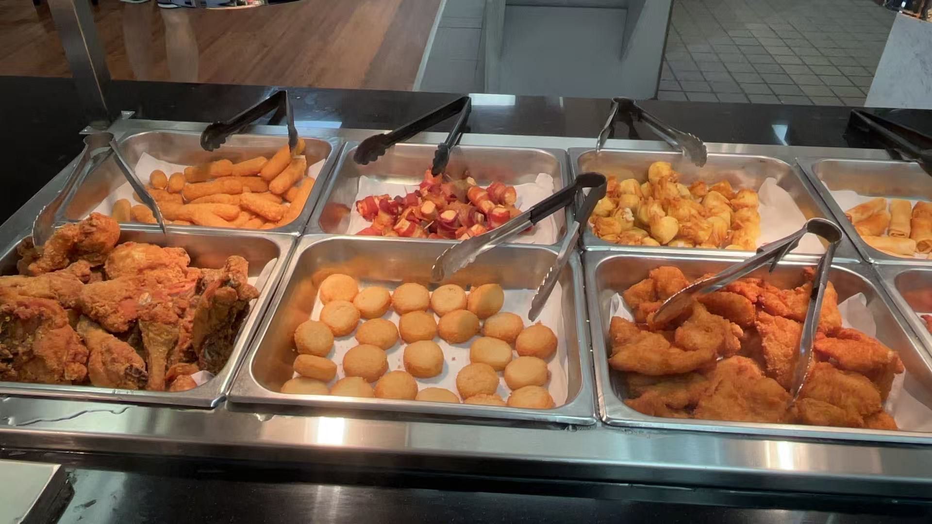 Buffet with various fried foods: chicken, nuggets, and tater tots, lit by overhead lighting.