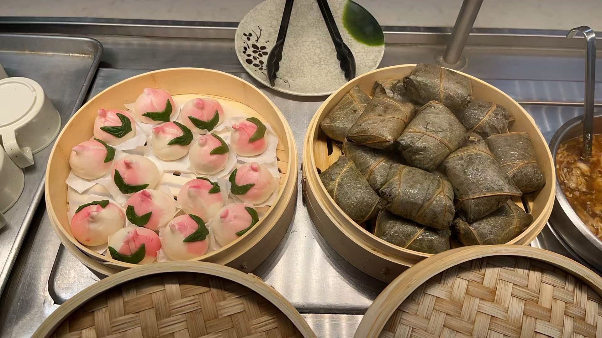 Peach-shaped buns and rice dumplings in bamboo steamers at a restaurant buffet.