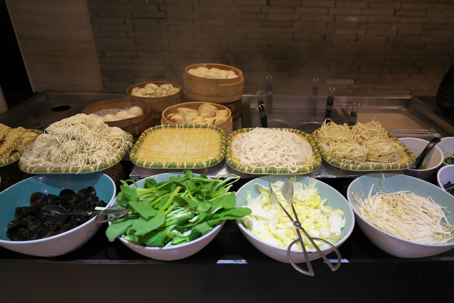 A buffet display of noodles, vegetables, and dumplings.