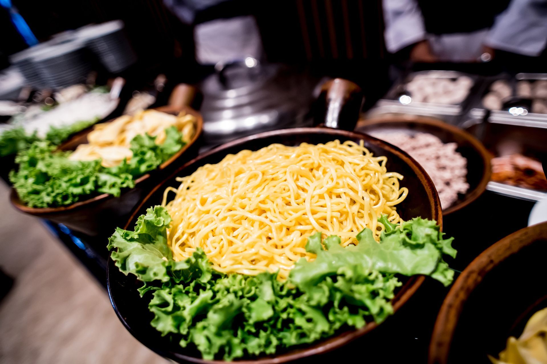 Buffet with bowls of yellow noodles, lettuce, and other food items.