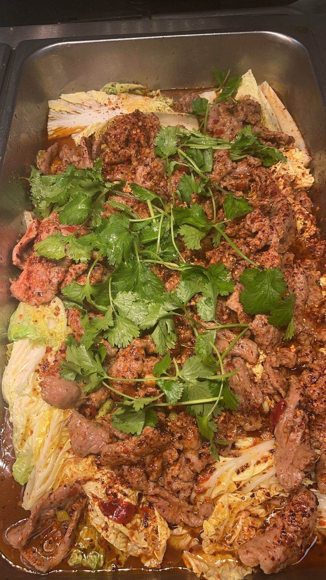 Tray of Chinese stir-fry with beef, cabbage, cilantro, and red chili oil.