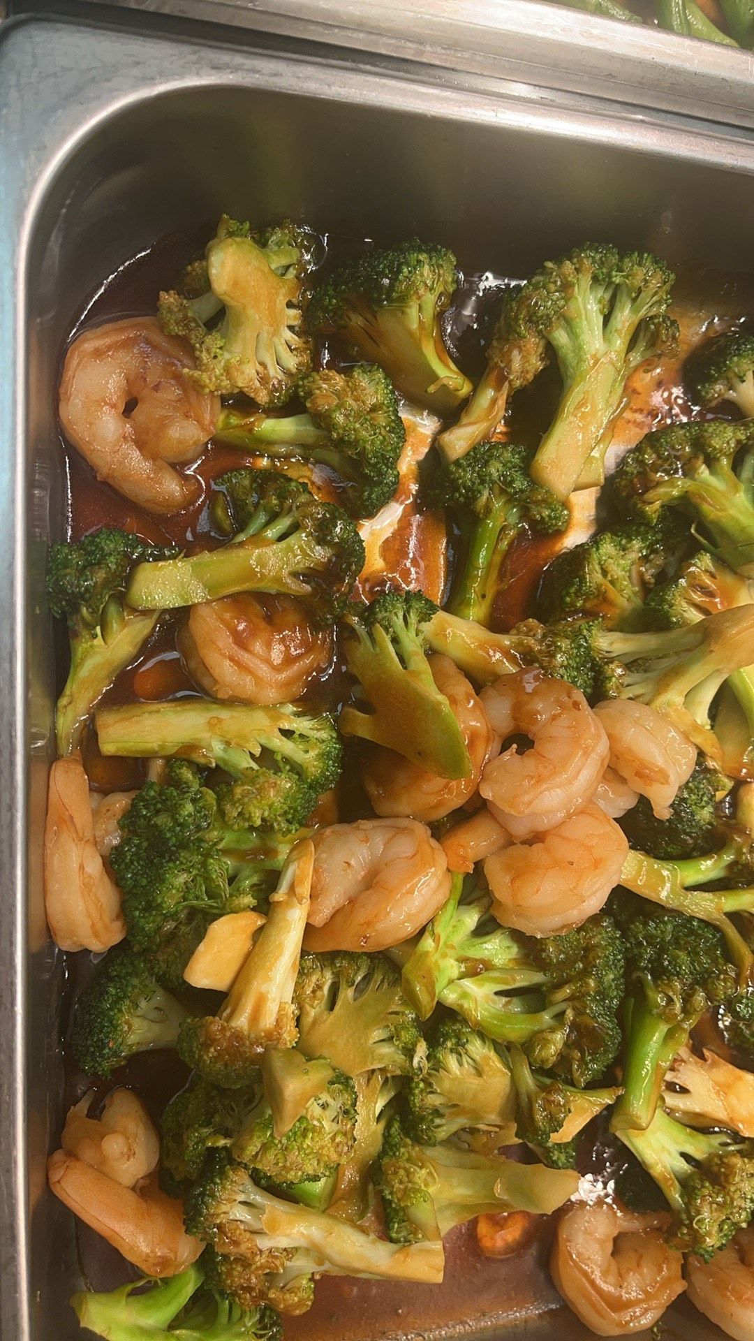 Shrimp and broccoli stir-fry in a metal serving tray, with brown sauce.
